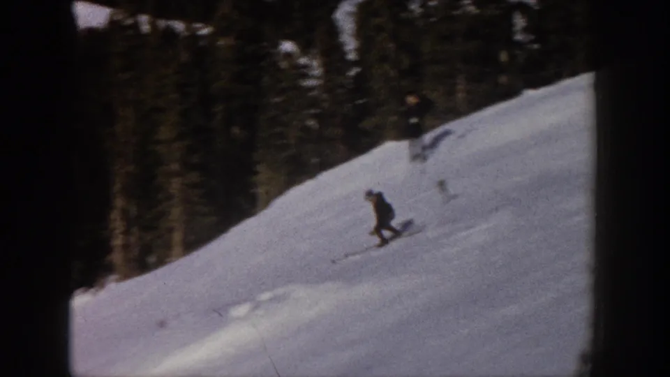 A distant skier in dark clothing bends into a cautious downhill turn on a snowy Aspen slope beneath evergreen trees.