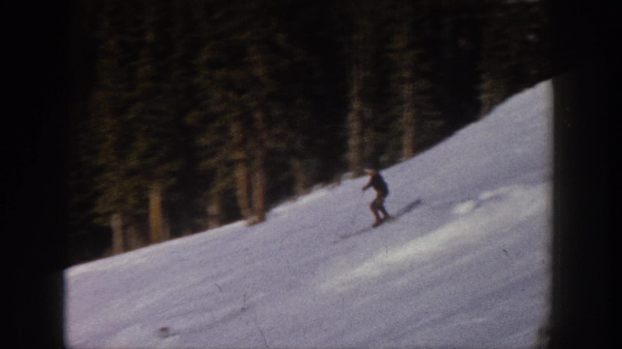 Lone skier crosses a snowy slope with dark evergreen trees behind.