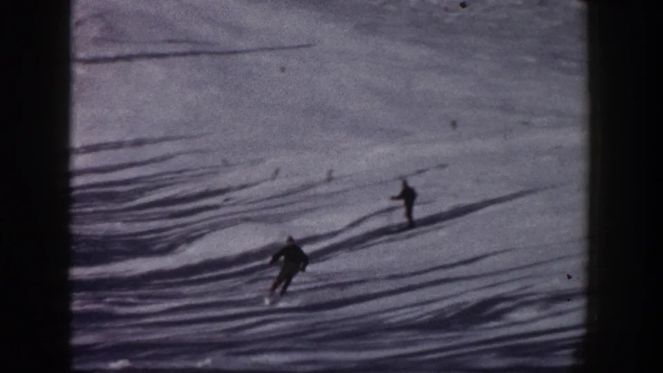 1961 Aspen 8mm frame showing skiers on a snow slope crossed by long tree shadows and dark frame edges.