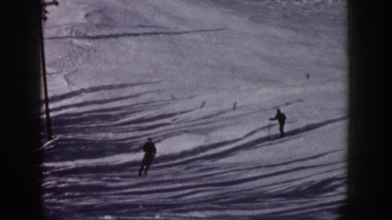 Distant adult skiers descend a snowy Aspen slope in 1961, framed by long shadows and the soft grain of color 8mm home-movie film.