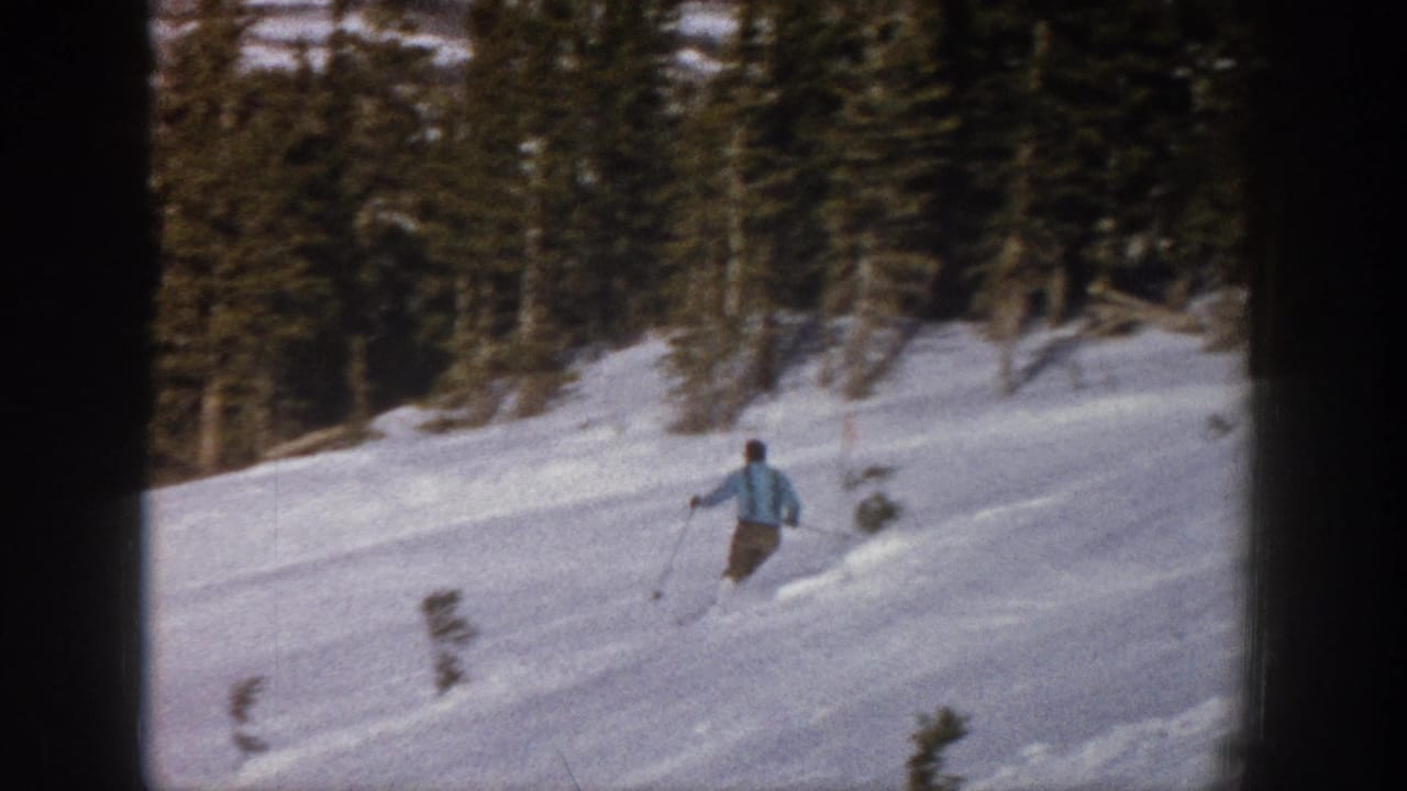 A distant skier in a light blue jacket skis downhill on a snowy Aspen, Colorado slope in 1961-era 8mm footage.
