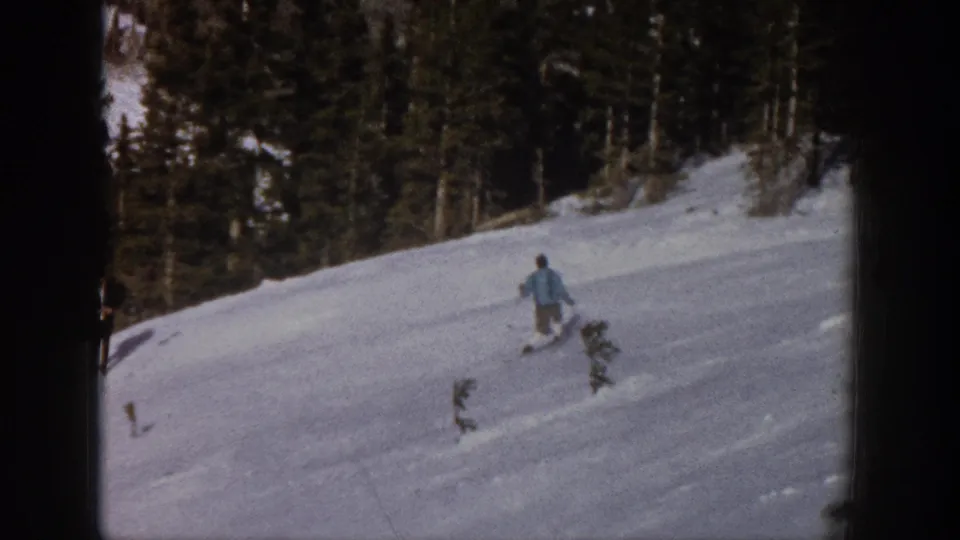 The skier moves farther downhill across open snow, framed by evergreen forest in Aspen, Colorado home-movie footage.