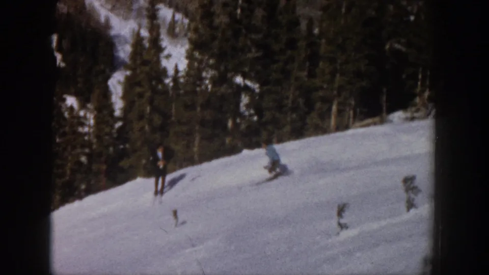A skier turns across the snowy Aspen slope while a second distant figure appears near the treeline in 1961 8mm footage.