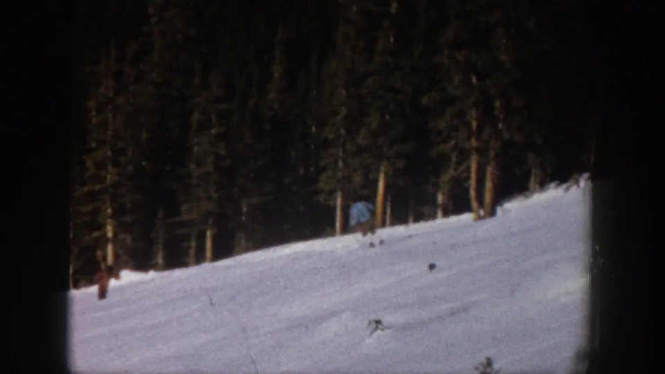 Distant skier on an Aspen snow slope in 1961, framed by a dark 8mm border and dense evergreen trees.