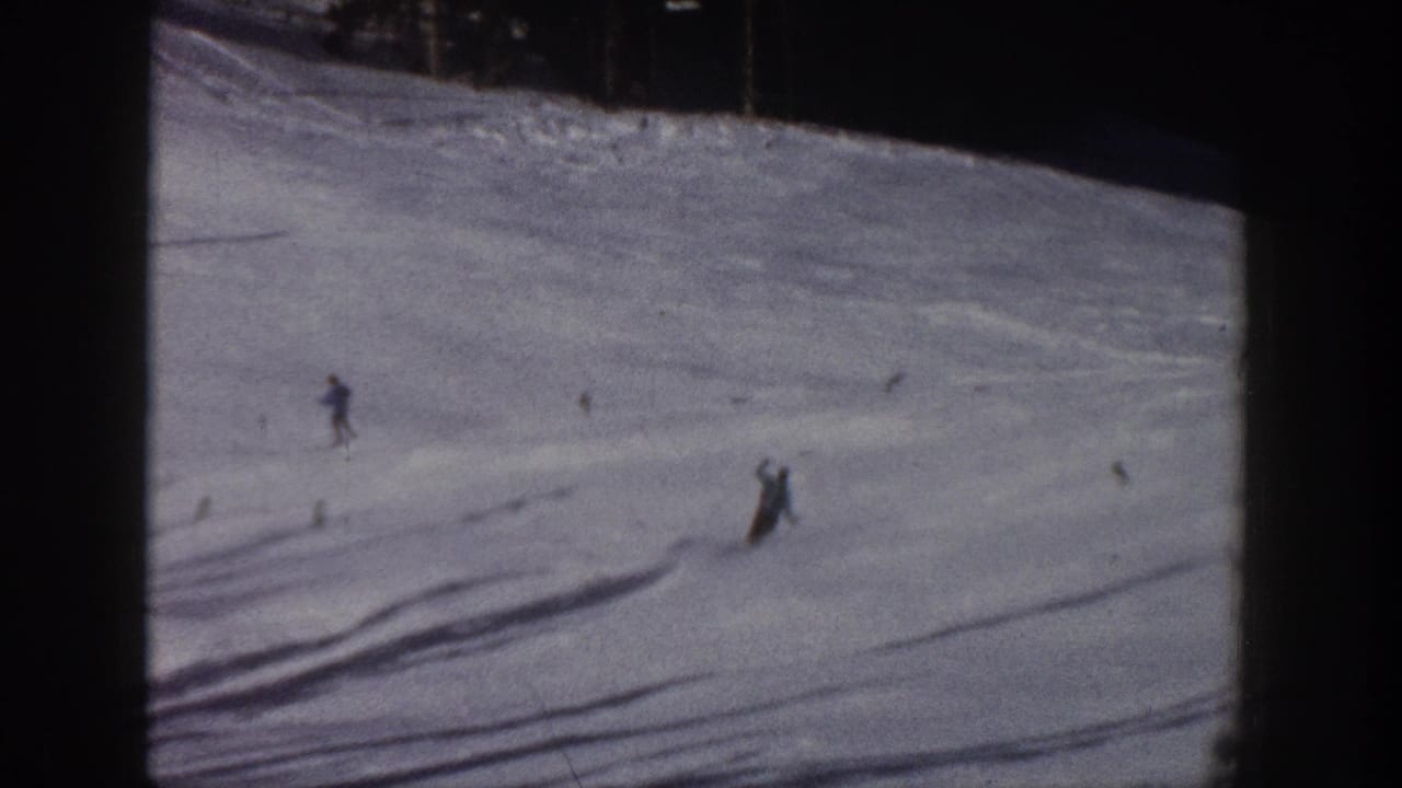 Distant skiers cross a sunlit snowy hill.