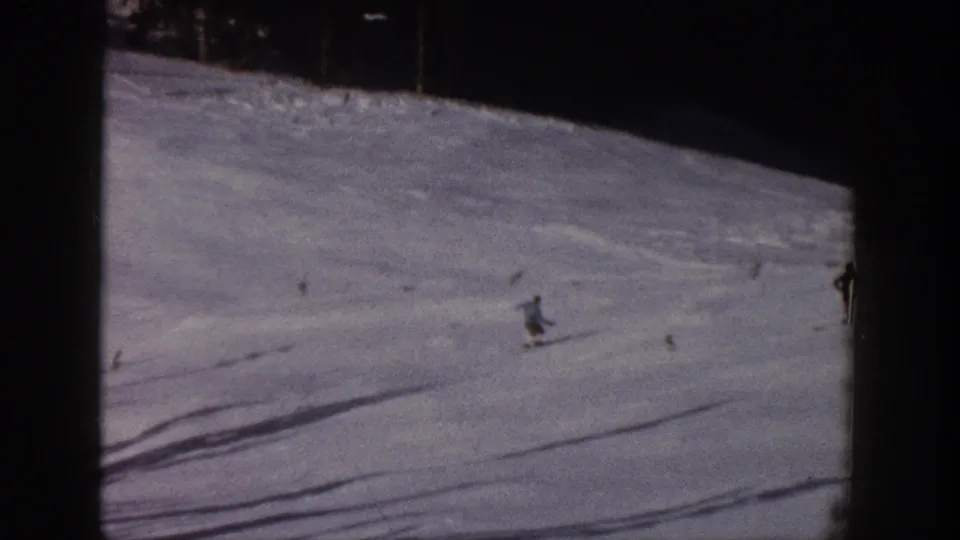 A skier crosses a broad Aspen ski slope in 1961 footage, with tree shadows and a few distant figures visible.