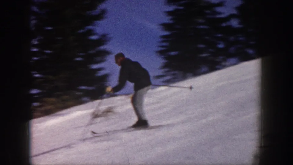 1961 Aspen frame showing a lone skier leaning into a turn on a snow-covered slope with dark trees behind.