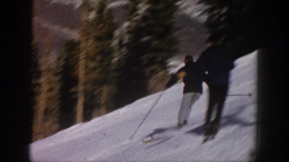 1961 Aspen frame showing the skier farther downhill beside evergreen trees on a snowy mountain slope.
