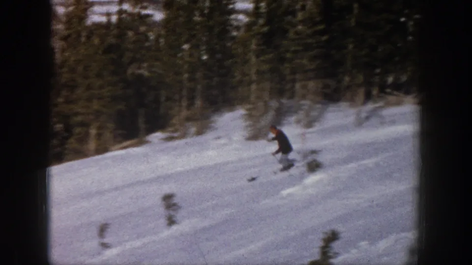 A distant skier in dark winter clothing moves down a snowy Aspen, Colorado slope in 1961 home-movie footage.