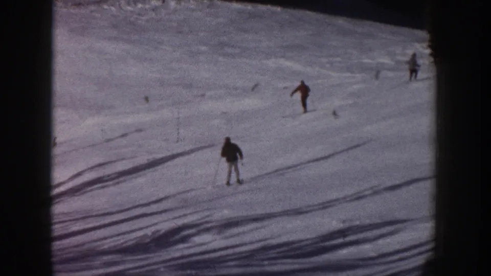 1961 Aspen 8mm frame with a dark-clad skier on the snowy run and other skiers higher on the slope.