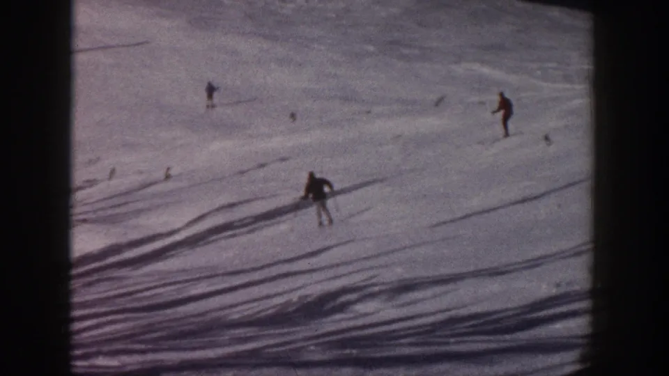 1961 Aspen home-movie frame showing a skier bending or recovering on the slope with other skiers above.