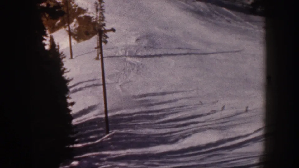 Aspen, Colorado 1961 8mm frame showing the edge of a ski slope, a pole, tree shadows, and faint skier traces in snow.