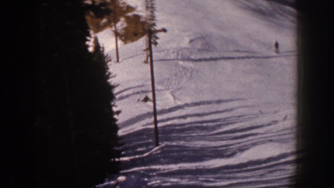 1961 Aspen home-movie frame showing distant skiers on a snowy mountain slope beside evergreen trees.