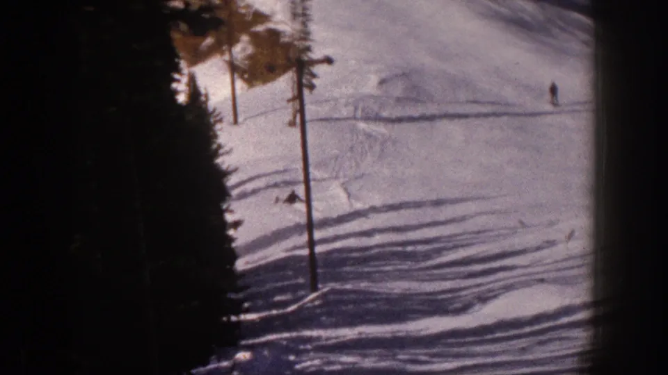 1961 Aspen home-movie frame showing distant skiers on a snowy mountain slope beside evergreen trees.