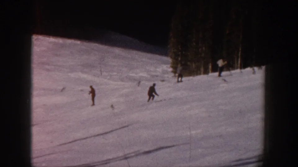 Distant skiers traverse an Aspen, Colorado snow slope in faded 8mm home-movie footage from 1961.