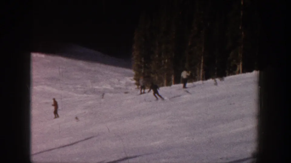 1961 Aspen ski-slope frame with distant skiers spread across a pale snowy hillside near evergreen woods.