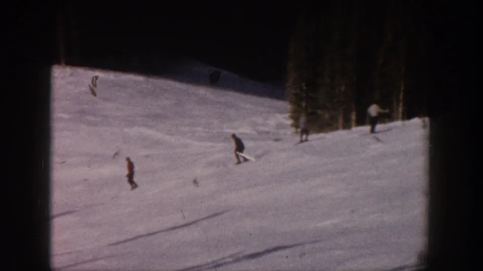 Faded 8mm frame from Aspen in 1961 showing skiers spaced across a snow-covered slope by evergreen trees.