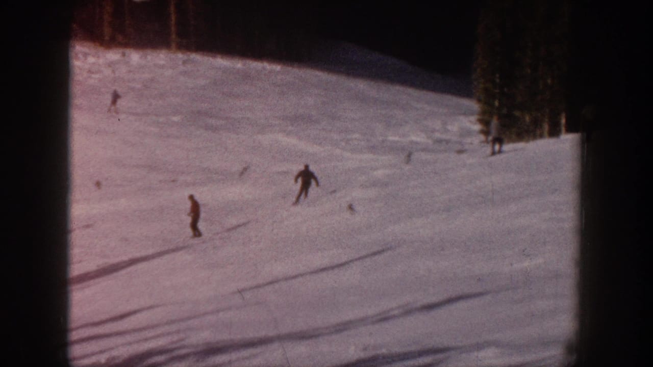 1961 Aspen home-movie frame showing distant skiers on a snow-covered run with pine trees and long shadows.