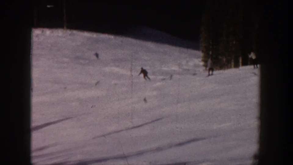Aspen ski vacation footage from 1961 showing a distant skier crossing a snowfield near tall evergreens.