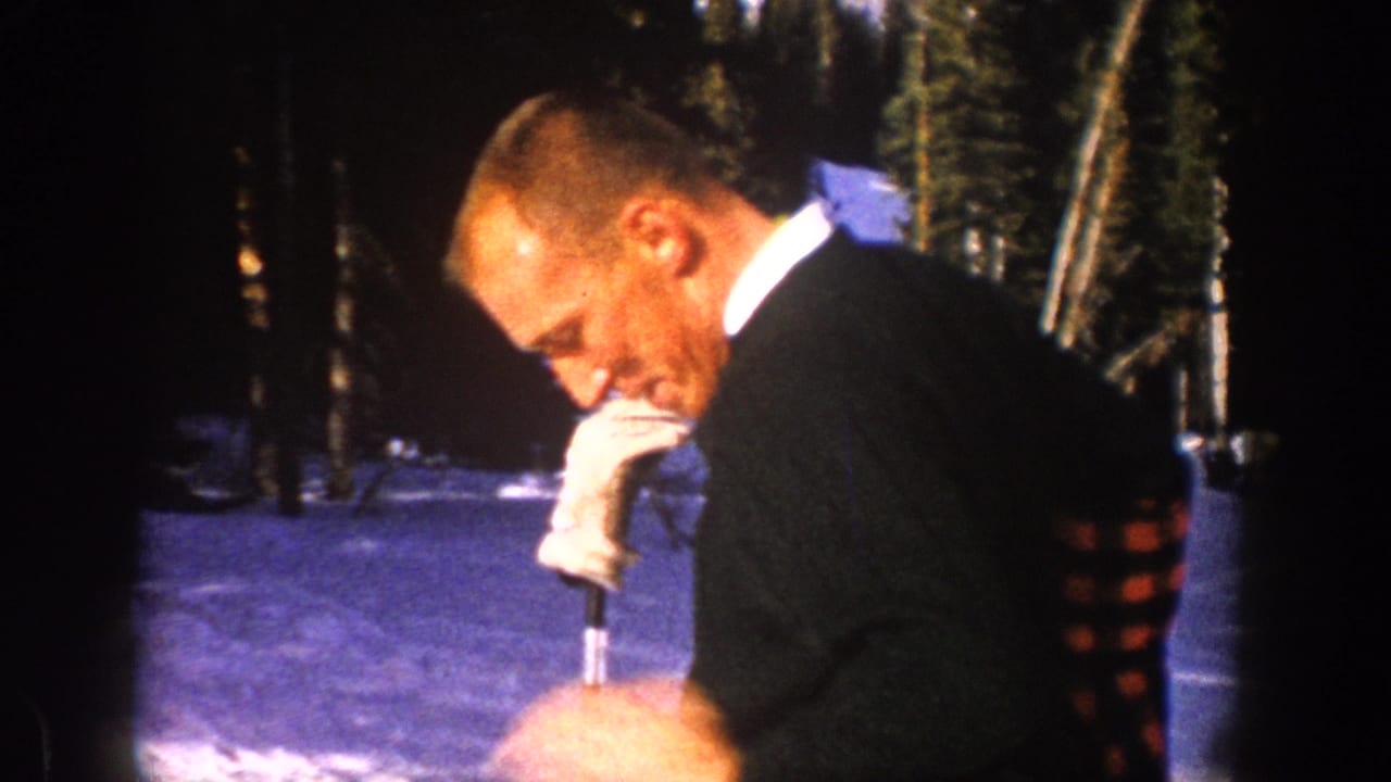 A man in snowy Aspen woods looks down as he draws a dark coat with plaid lining around his shoulders.