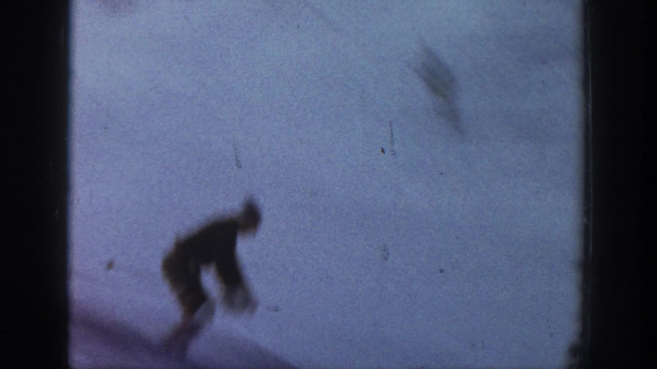 A distant skier in dark clothing bends forward on snow in faded 1961 Aspen 8mm home-movie footage.