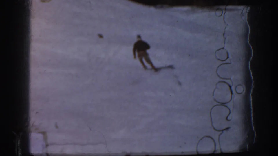 A distant skier moves down a pale snowy Aspen hillside in soft, scratched 8mm home-movie footage.