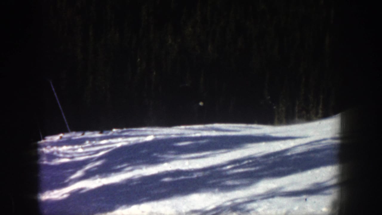 Snowy ski slope with dark evergreen forest and film-frame borders.