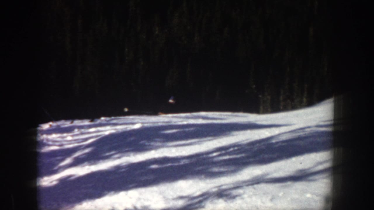 1961 Aspen footage frame with a bright snowfield, forest backdrop, long shadows, and visible 8mm contact-sheet borders.
