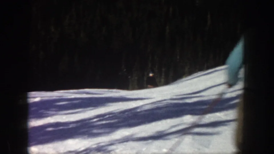 1961 Aspen frame with part of a skier in a light blue jacket entering the snowy slope against a dark forest backdrop.