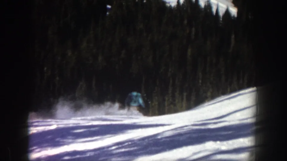 The skier is mostly hidden by a burst of snow while continuing downhill on the Aspen slope, with trees and shadowed snow visible.