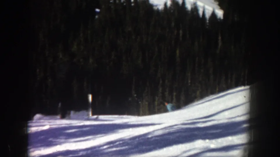 Near the end of the 1961 Aspen shot, the skier moves toward the right edge while the camera holds the snowy slope and dark forest.