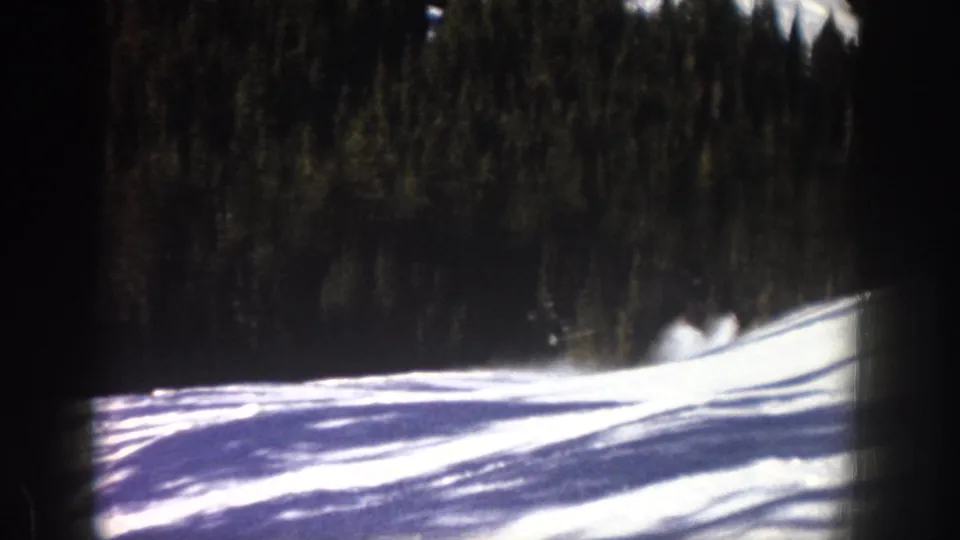 1961 Aspen ski footage frame with snow, forest backdrop, strong shadows, and possible skier movement near the right side.