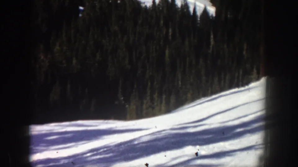 1961 Aspen frame showing an open snowy downhill slope, dark evergreen trees, and pronounced film-frame borders.