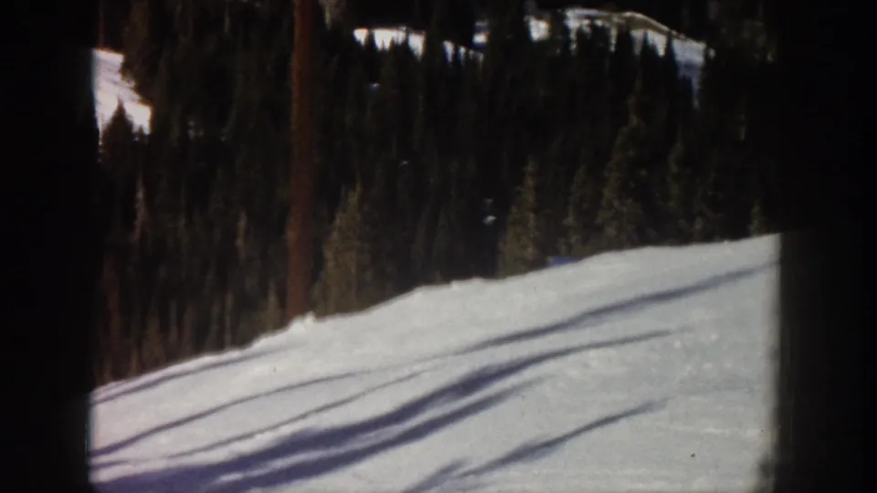 1961 Aspen home-movie frame after the skier has left view, showing a snowy slope and dark evergreen trees.
