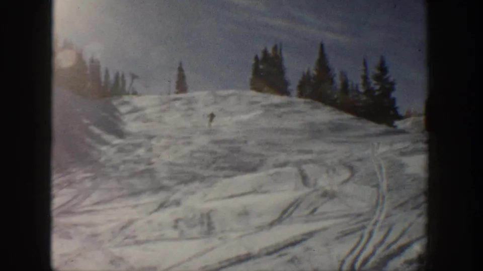 A distant skier descends a snowy Aspen, Colorado slope in 1961, with pine trees along the ridge and ski tracks in the foreground.