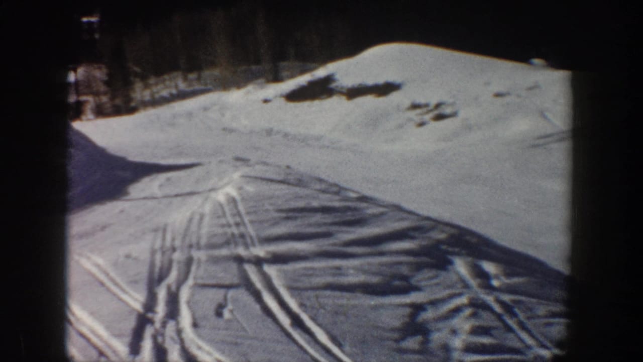 Snowy Aspen hillside with parallel ski tracks, dark tree line, and long shadows visible in the 8mm frame.