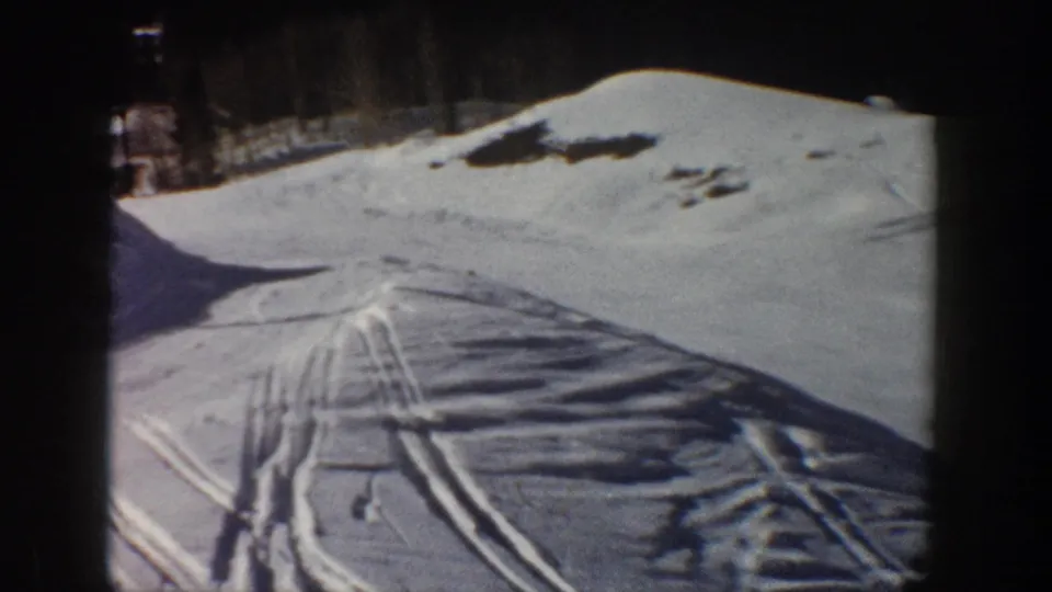 Snowy Aspen hillside with parallel ski tracks, dark tree line, and long shadows visible in the 8mm frame.