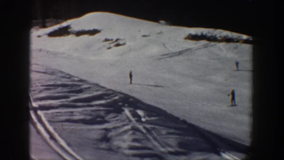 1961 Aspen frame showing distant skiers on a broad snowy hillside, with ski tracks crossing the foreground.