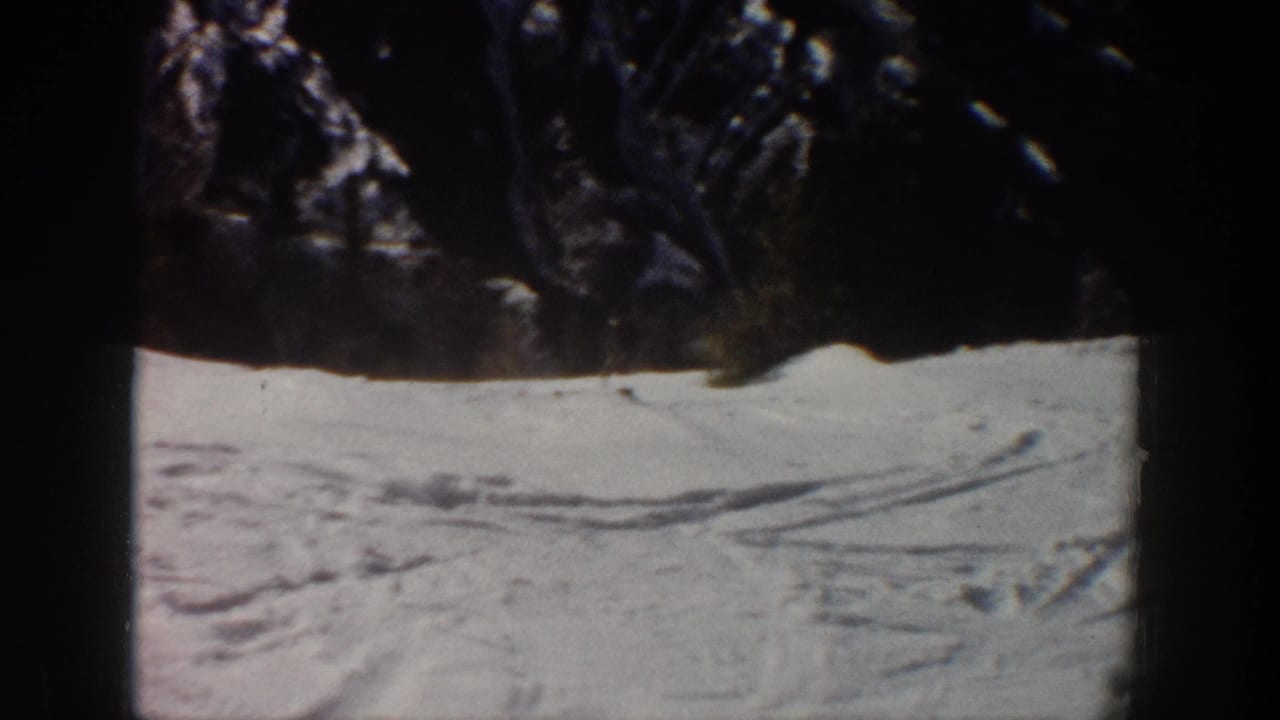 Dark wooded foreground frames a snowy Aspen ski slope with visible tracks in 1961 home-movie footage.