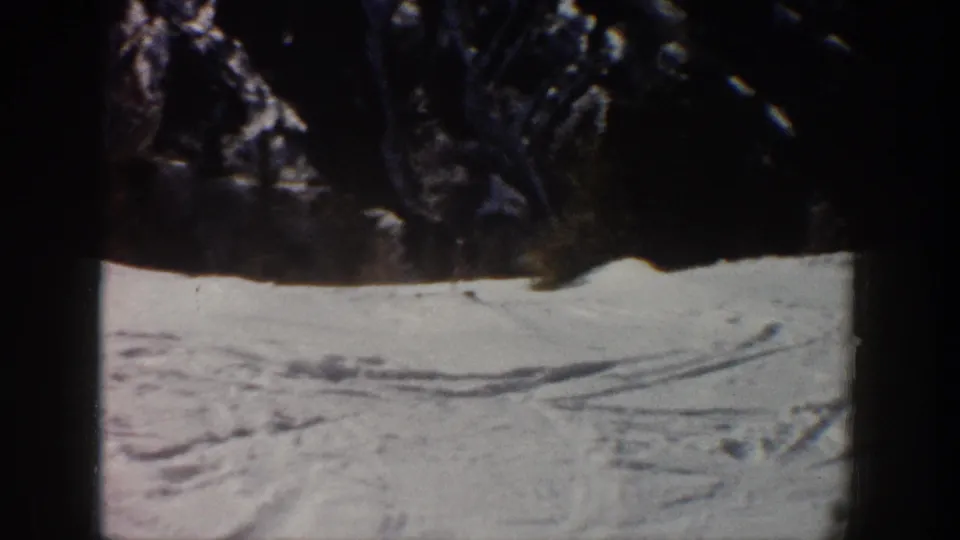 Dark wooded foreground frames a snowy Aspen ski slope with visible tracks in 1961 home-movie footage.