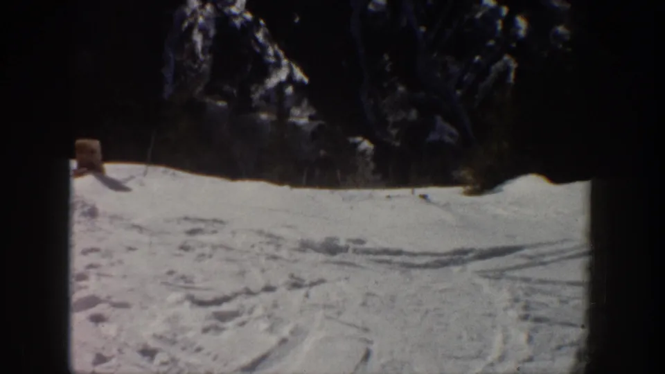 Snow-covered Aspen slope with ski tracks and dark evergreen trees, seen in soft 1961 8mm color footage.