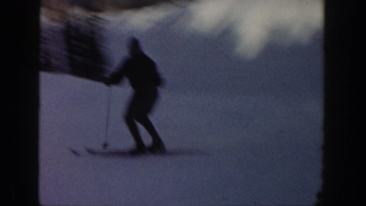 1961 Aspen ski-vacation frame with a silhouetted skier using poles on bright snow near dark evergreens.