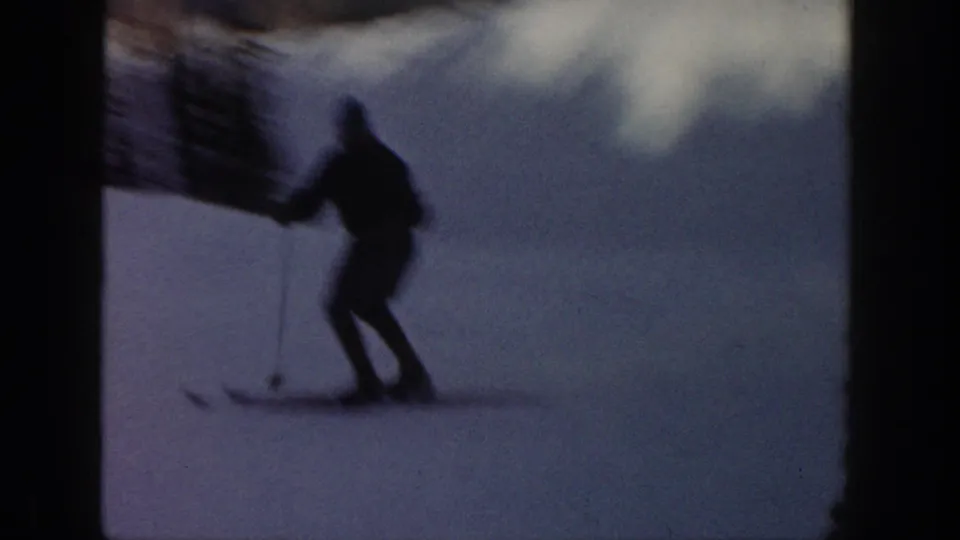 1961 Aspen ski-vacation frame with a silhouetted skier using poles on bright snow near dark evergreens.