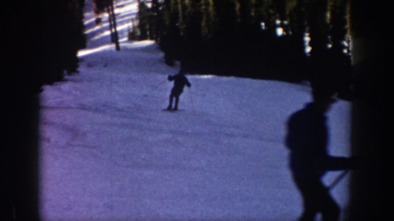 1961 Aspen 8mm frame showing a distant skier descending a snowy slope with dark evergreen trees behind.