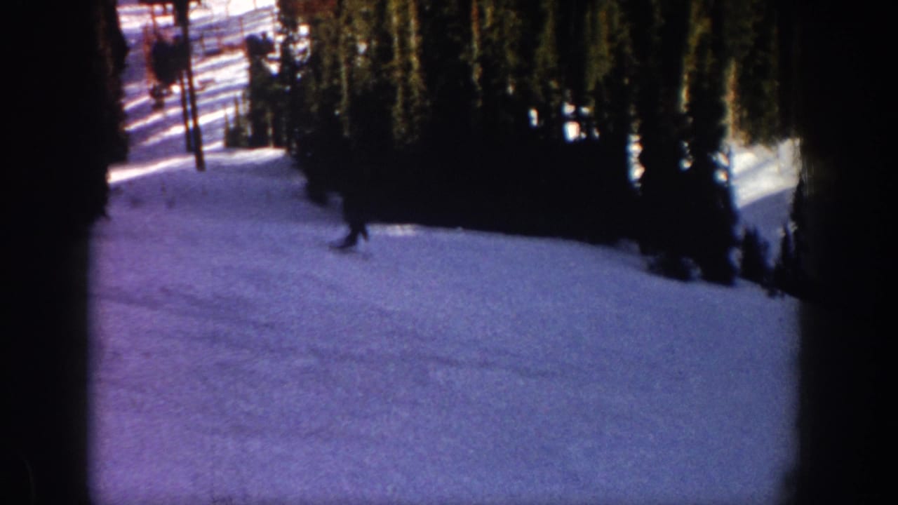 1961 Aspen, Colorado home-movie frame showing a distant skier crossing a snowy wooded slope.