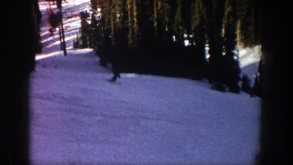 1961 Aspen, Colorado home-movie frame showing a distant skier crossing a snowy wooded slope.