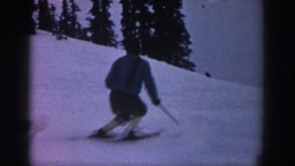 Close view of a skier turning downhill on a wooded Aspen, Colorado snow slope in 1961 home-movie footage.