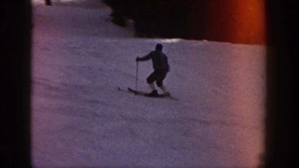 1961 Aspen home-movie frame showing a skier descending a snowy slope, with visible film edge and reddish light leak.