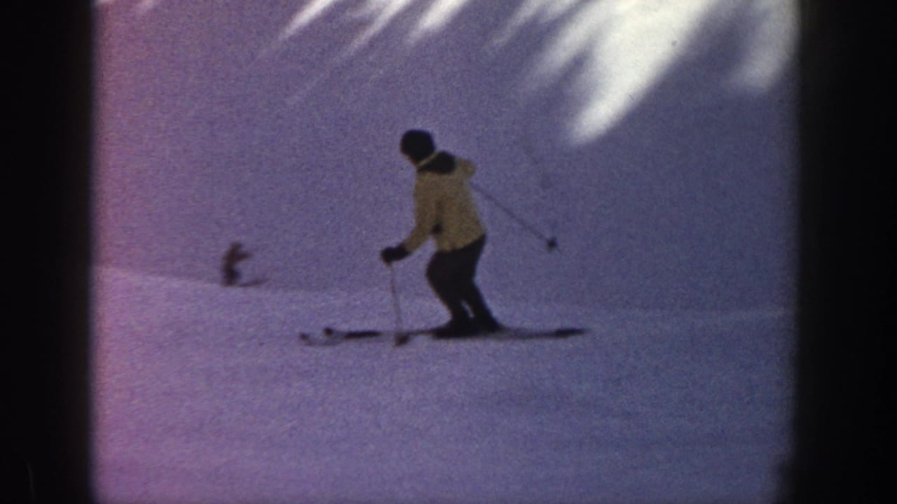 Skier descends a snowy slope while another skier appears in the distance.