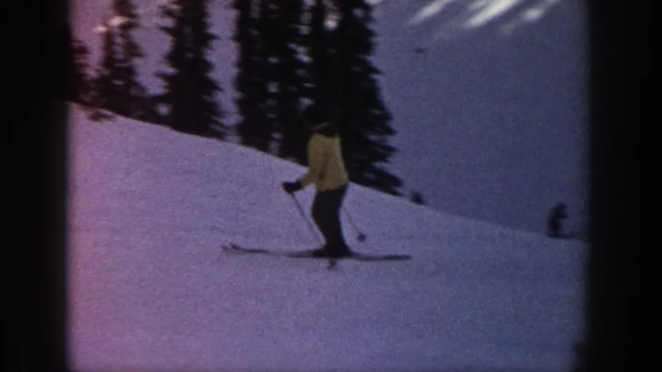 1961 Aspen home-movie frame showing a skier on a snow-covered incline with dark evergreen trees behind.